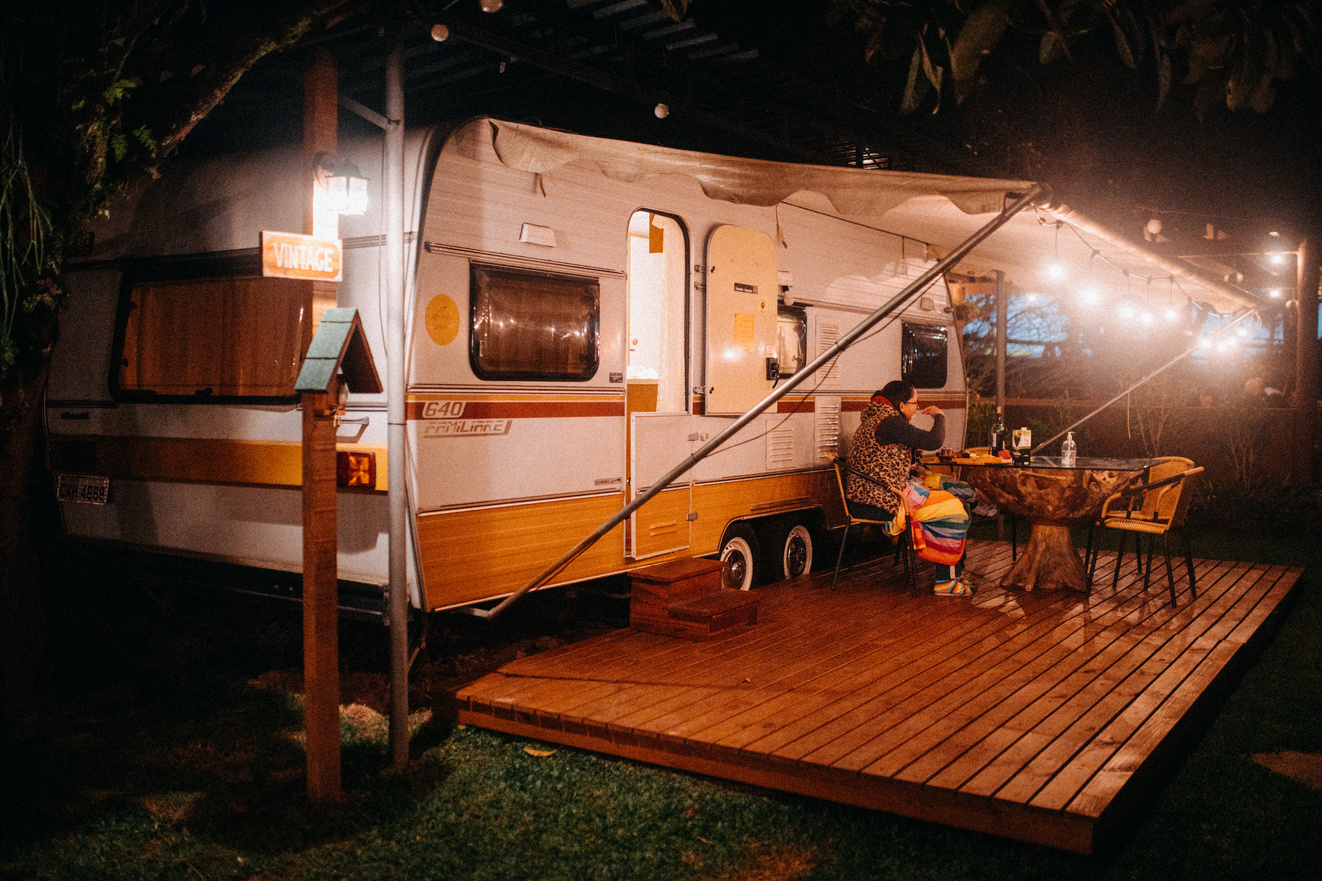 Traveler at table against caravan illuminated by lights in campsite